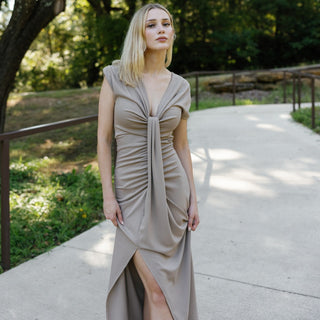 Woman in a beige dress standing on a path with greenery in the background