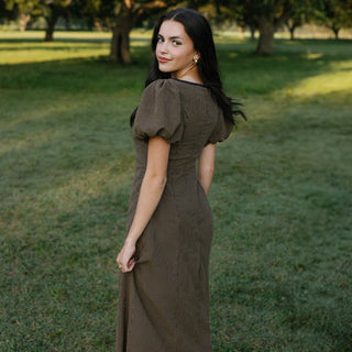 Woman in a brown dress standing in a grassy field