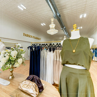 Fashion store interior with mannequin wearing a green outfit, hanging dresses, and a chandelier.