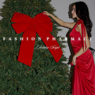 Woman in a red dress standing next to a Christmas tree with a large red bow, with 'Fashion Pharmacy' branding.