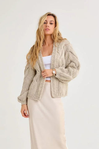 Woman wearing a beige cardigan and long beige skirt on a white background