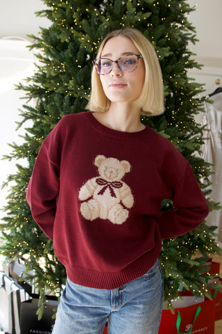 Person wearing a red sweater with a teddy bear design in front of a decorated Christmas tree.
